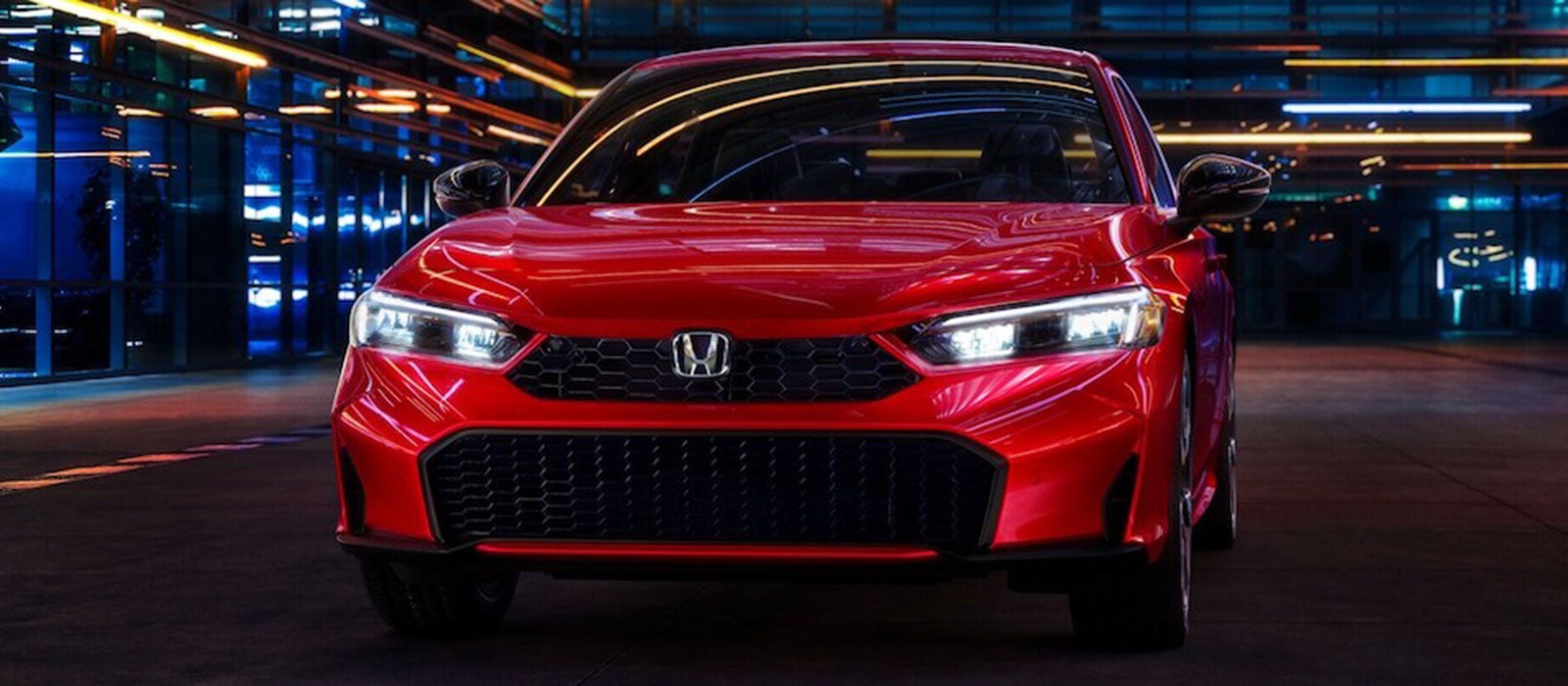 The front of a red 2026 Honda Civic Sport Touring Hybrid with its headlights on