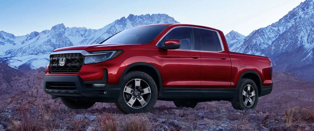 A red 2026 Honda Ridgeline truck parked in front of snowy mountains