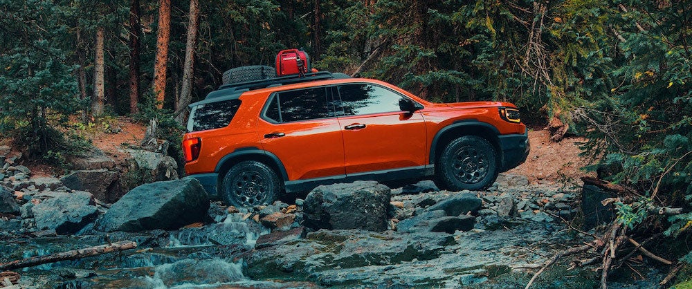 A side view of an orange 2026 Honda Passport as it crosses a rocky stream